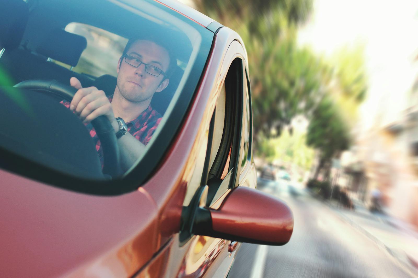 A man driving fast through a city street in a red car, showcasing motion and focus. auto